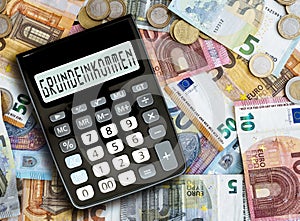 German word GRUNDEINKOMMEN basic income written on display of pocket calculator against cash money on table