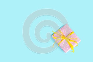 Top view of a gift box wrapped in pink dotted paper and tied yellow bow over light blue background.