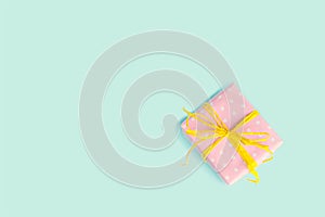Top view of a gift box wrapped in pink dotted paper and tied yellow bow over light blue background. Vintage effect.