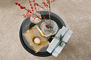Top view of gift boxes tied with an emerald ribbon with a sprig of spruce, a candle, a vase of red berries and a gold tray. Lay fl