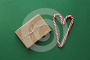 Top view. Gift Kraft Brown Color Box and Candy Canes Red and White in Heart Shape Lies on the Green Background, View From the Top