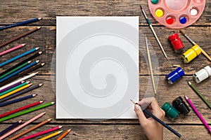 Top view of Girl hand drawing, Empty white canvas frame and colorful pencils on white wooden table