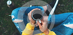 Top view girl holding in hands cup of hot tea on green grass in outdoors nature park, beautiful woman hipster enjoy drinking cup