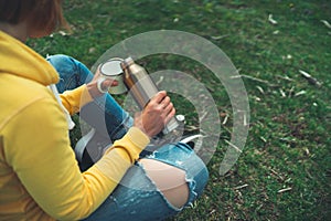 Top view girl holding in hands cup of hot tea on green grass in outdoors nature park, beautiful woman hipster enjoy drinking cup