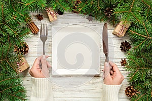 Top view girl holds fork and knife in hand and is ready to eat. Empty white square plate on wooden christmas background. holiday d