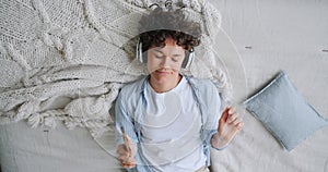 Top view of girl lying on bed enjoying music in headphones watching smartphone