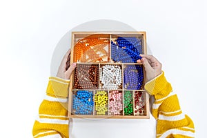 Top view of girls hand is sorting a puzzle of colored plastic beads in montessori school