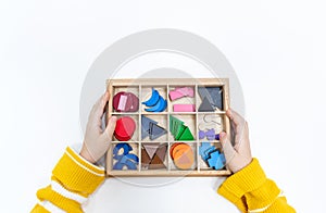 Top view of girls hand is sorting a puzzle of colored wooden geometric shapes in montessori school