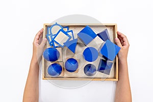 Top view of girls hand is sorting a puzzle of colored wooden geometric shapes in montessori school