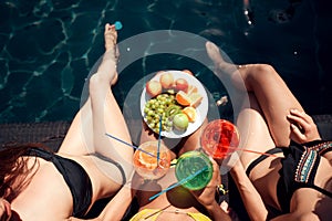 Top view. Girls in swimsuits eat fruits and drink cocktails drinks in swimming pool in summertime.