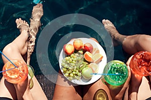 Top view. Girls in swimsuits eat fruits and drink cocktails in swimming pool in summertime.