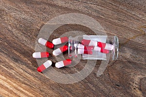 Top view of glass  bottle and red and pink antibiotic pills on wooden table