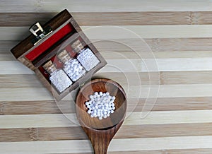 Top view of Glass Bottles of homeopathic pills in a retro styled on old wooden box and globules in wood spoon on wood background
