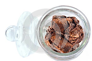 Top view of a glass cookie jar with chocolate brownie pieces. Glass lid open and propped against the side of container