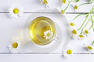 Top view of a glass cup of chamomile tea and chamomile flowers.