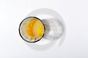 Top view of glass cup and fresh broken egg yolks in it on the white kitchen table.Empty space