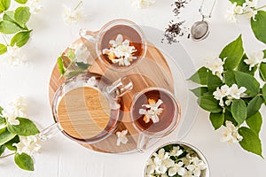 Top view of glass cups and teapot with jasmine tea and jasmine flowers on a round wooden board. white background