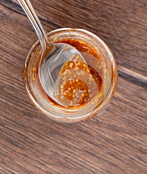 Top view of glass jar with bavarian mustard and spoon on wooden background.