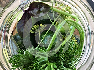 Top view of a glass jar with cucumbers and herbs