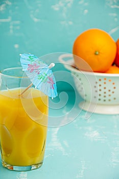 Top view of glass with juice and blue umbrella on drainer with oranges on table and blue background,