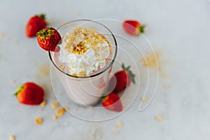 Top view of a glass of a strawberry milkshake surrounded by strawberries with cream on top