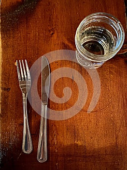 Top view of the glass of water, knife, and fork on the wooden tabl