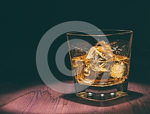 Top of view of glass of whiskey with ice cubes on wood table, warm atmosphere, time of relax with whisky