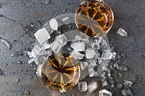 Top view of glasses with brandy and pieces of ice on gray surface.Party drinks