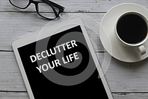 Top view of glasses, a cup of coffee and tablet written with Declutter Your Life on white wooden background