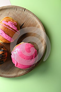 Top view of glazed donuts on a wooden plate on a pastel green background, top view with free space for your text