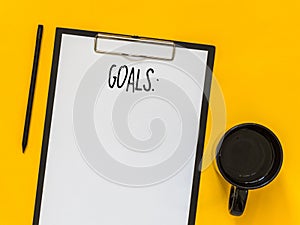 Top view goals list with notebook, cup of coffee on yellow background with blank space for text. Flat lay. Copy space.