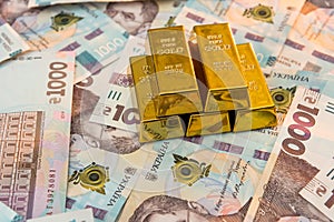 Top view of gold bars lying on a background of Ukrainian money. UAH. Save and money concept