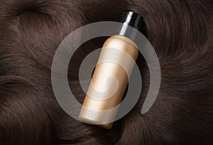 Top view of golden bottle of cosmetic product on dark brunette curls. Hair colouring and salon professional care. AI