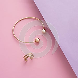 Top view of golden bracelet and ring on slanted pink and purple paper with copy space