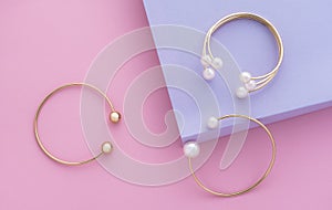 Top view of golden bracelets with pearls on pink and purple paper background with copy space