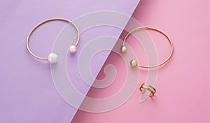 Top view of golden with pearl bracelet and ring on pink and purple slanted paper background