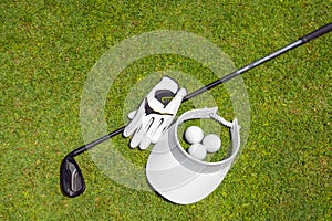 Top view of golf equipment on green grass on a golf course. Flat lay of golf club, balls, glove and cap