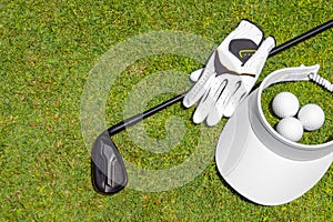 Top view of golf equipment on green grass on a golf course. Flat lay of golf club, balls, glove and cap