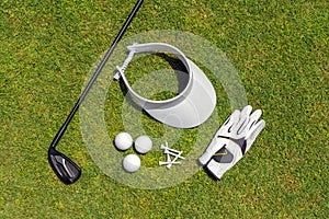 Top view of golf equipment on green grass on a golf course. Flat lay of golf club, balls, glove, tees and cap