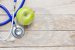 Top view green apple with blue stethoscope on wood table background.