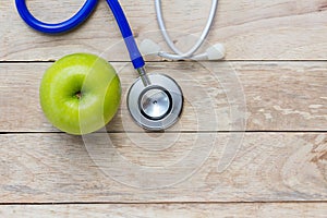 Top view green apple with blue stethoscope on wood table background.