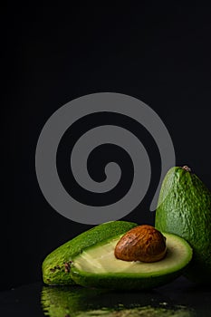 Top view of green avocados, one cut, on wet black slate, with reflection, on black background, vertically,