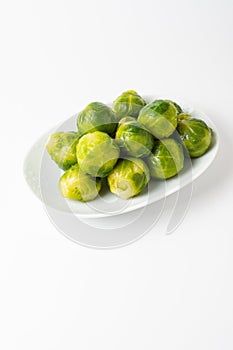 Top view of green Brussels sprouts on white plate, white background, vertical