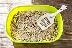 Top view of green cat litter box with wooden pellets and scoop on a brown wooden floor. Plastic cat toilet tray. Toilet for pets