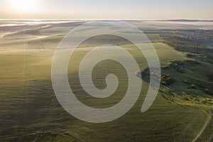 Top view of green cultivated hills and green trees in foggy valley. Spring misty landscape panorama at dawn