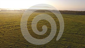 Top view of green hills and blue sky with low clouds above them. Footage. Foggy horizon with morning sun and green field