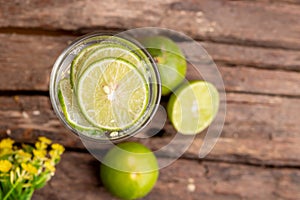 Top view green lime sliced in the soda water and glass place on the wooden table with yellow flowers
