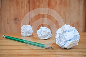 Top view of green pencil with many white crumpled paper ball put on wooden floor.