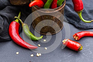 Top view of the green and red hot chili peppers in a rusty cup with cloth on a dark tabletop