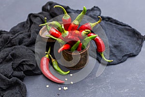 Top view of the green and red hot chili peppers in a rusty cup with cloth on a dark tabletop